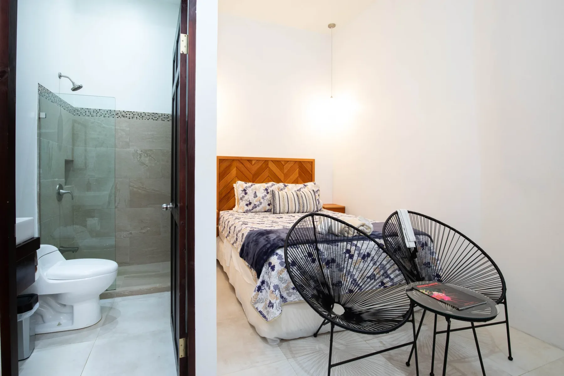A bedroom with a patterned bed and two wire-frame chairs beside the bathroom.