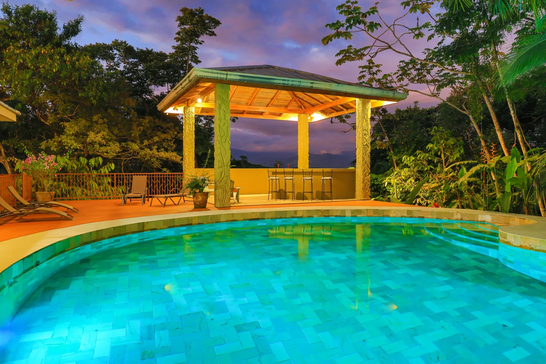 Una piscina junto a una zona exterior cubierta con asientos al anochecer.