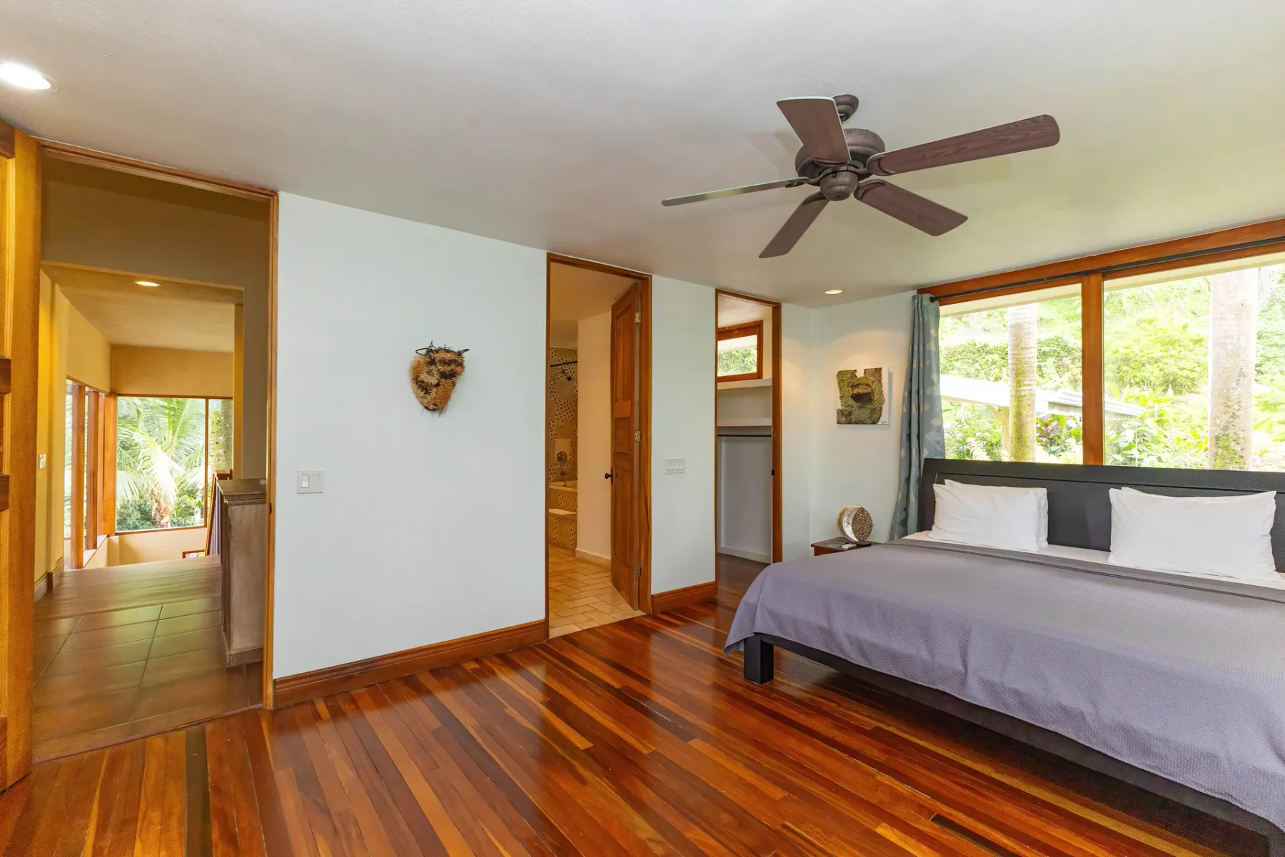 Dormitorio luminoso con una cama junto a amplias ventanas y suelo de madera pulida.