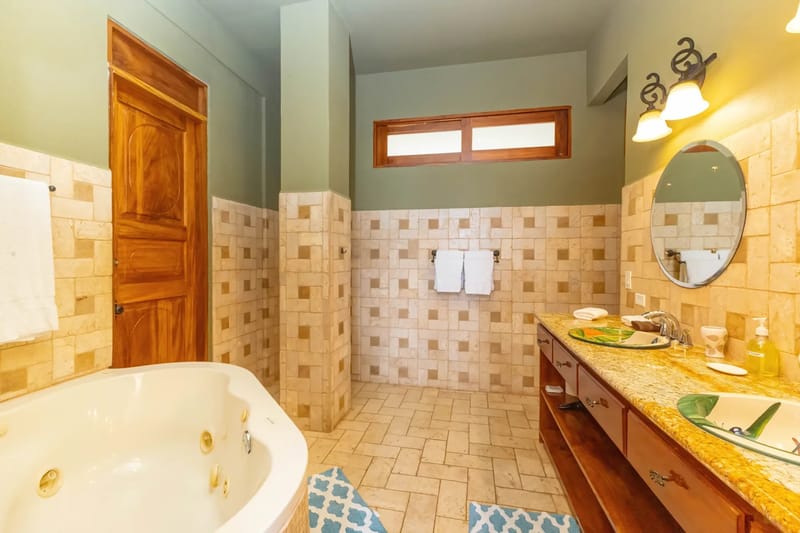The Rainforest Estate · 9. This spacious bathroom features a large jetted tub, a double vanity with granite countertop and decorative sinks, tiled walls and floor, and natural light from a high horizontal window.