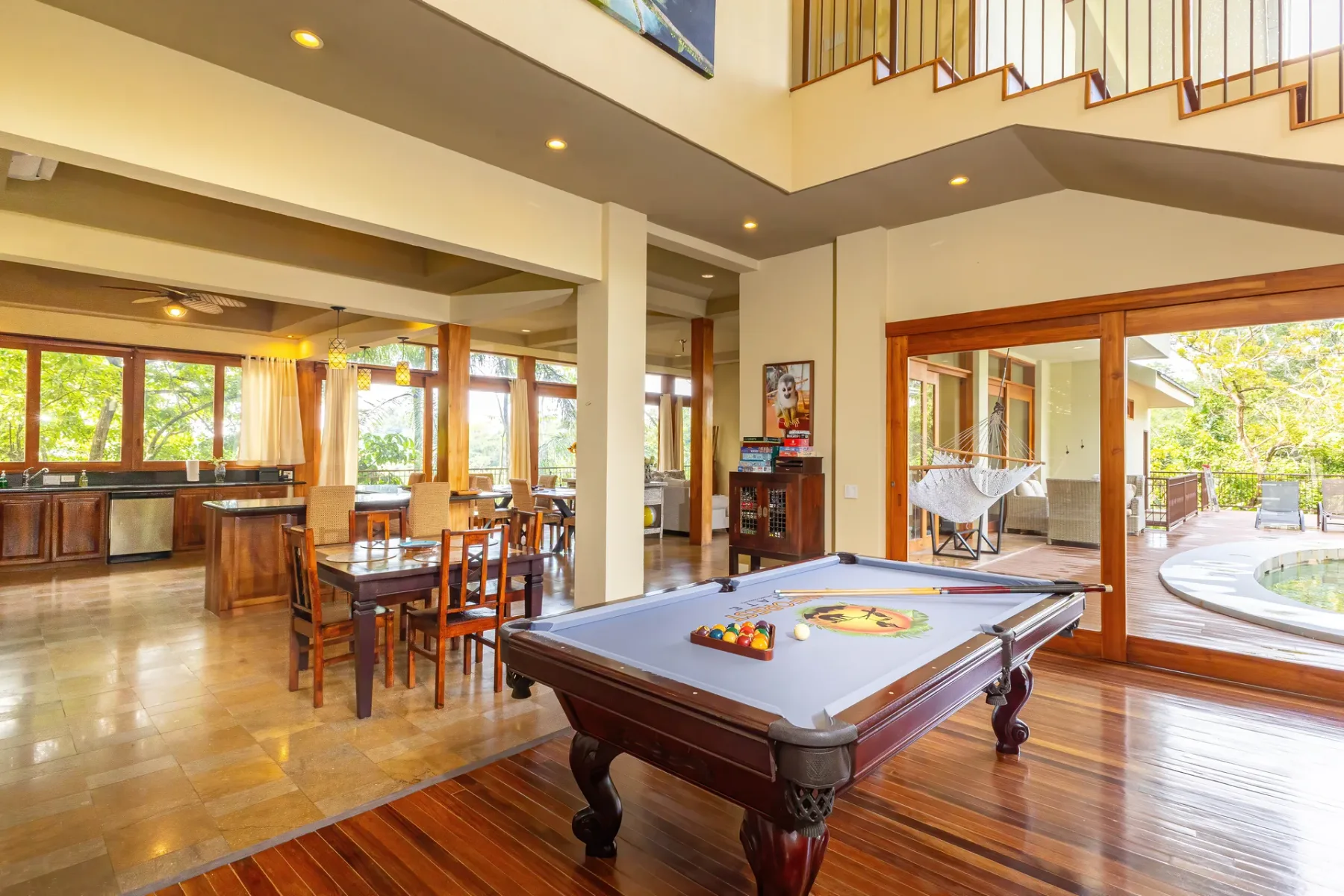Una zona abierta de estar y comedor cuenta con una mesa de billar y grandes ventanas.