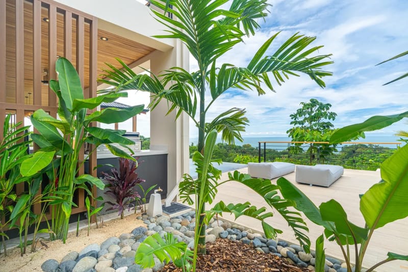 Villa del Cielo · 9. An outdoor terrace with an integrated kitchen and lounge seating is surrounded by tropical plants, framing views of an infinity pool, jungle, and the Pacific Ocean.