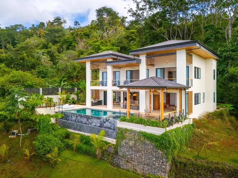 Villa del Cielo · 10. A modern two-story villa featuring white facades, wooden accents, multi-level terraces, an infinity pool with an adjacent jacuzzi, and a covered palapa, all set against a dense tropical jungle hillside.