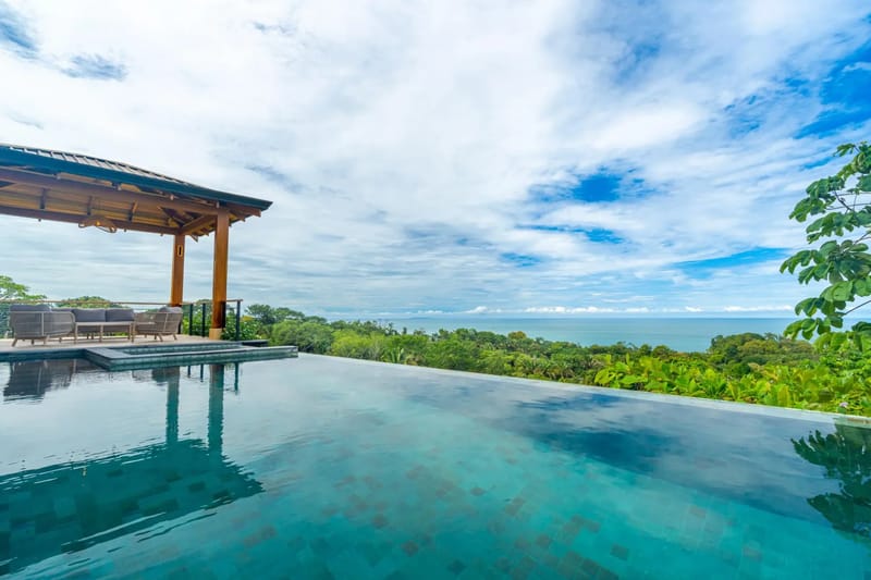 Villa del Cielo · 14. An infinity pool with a shaded palapa lounge area extends toward the Pacific Ocean and lush jungle under an open sky.