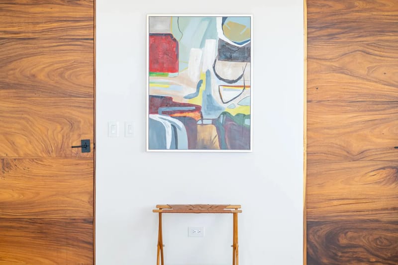 Villa del Cielo · 8. Natural wood doors with distinctive grain frame a white wall featuring abstract art and a woven leather luggage rack, adding a warm, contemporary accent to the interior.