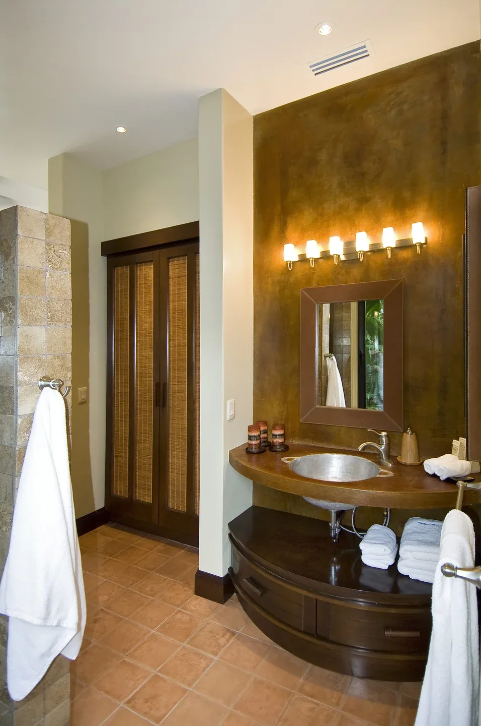 A bathroom vanity with a mirror and sink stands beside a tiled shower area.