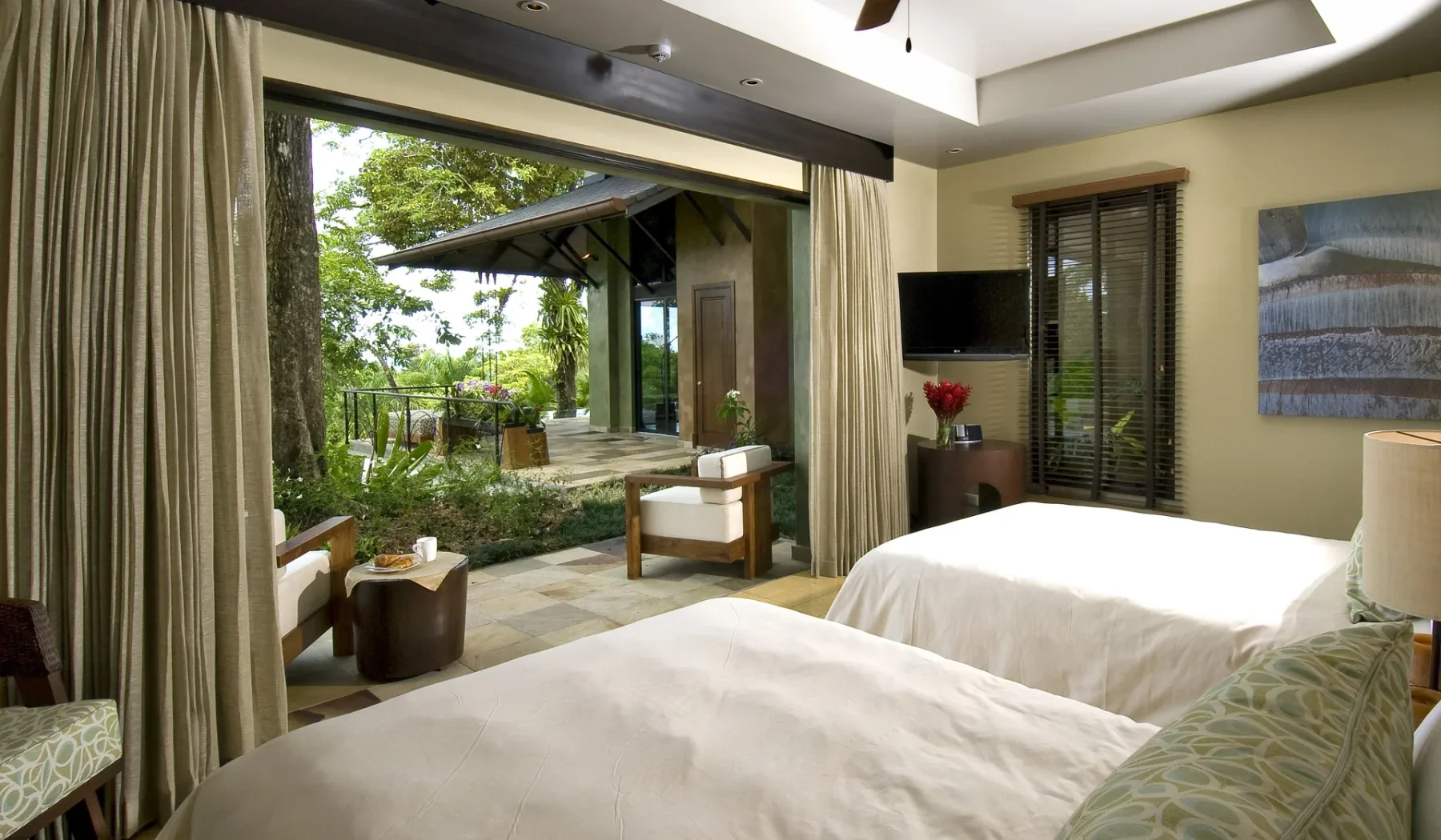 A bedroom with two beds and an open view toward a garden patio.