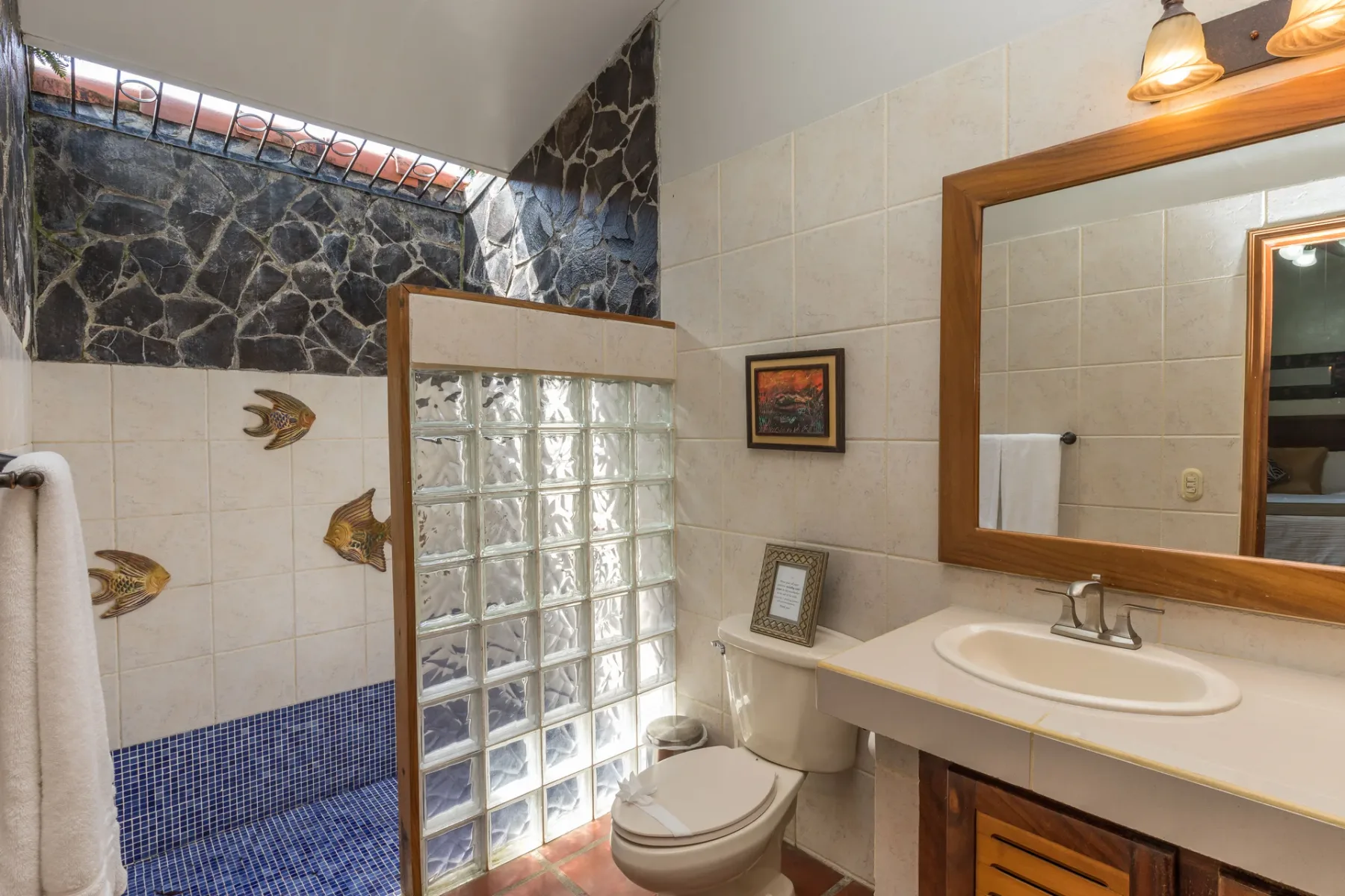 Un baño alicatado con una mampara de bloques de vidrio, inodoro y lavabo.