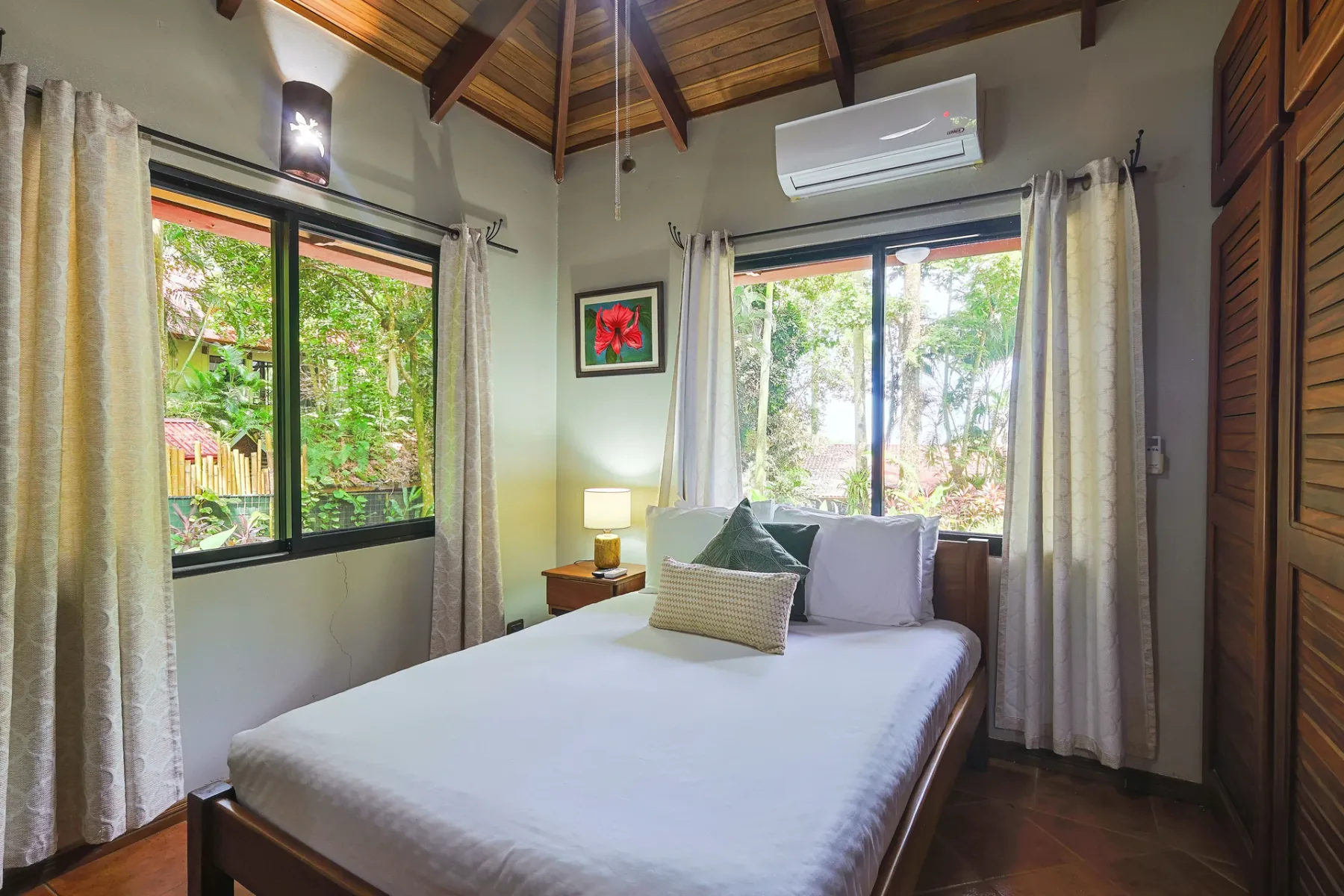 Un dormitorio con una cama, ventanas con cortinas y techo abovedado de madera.