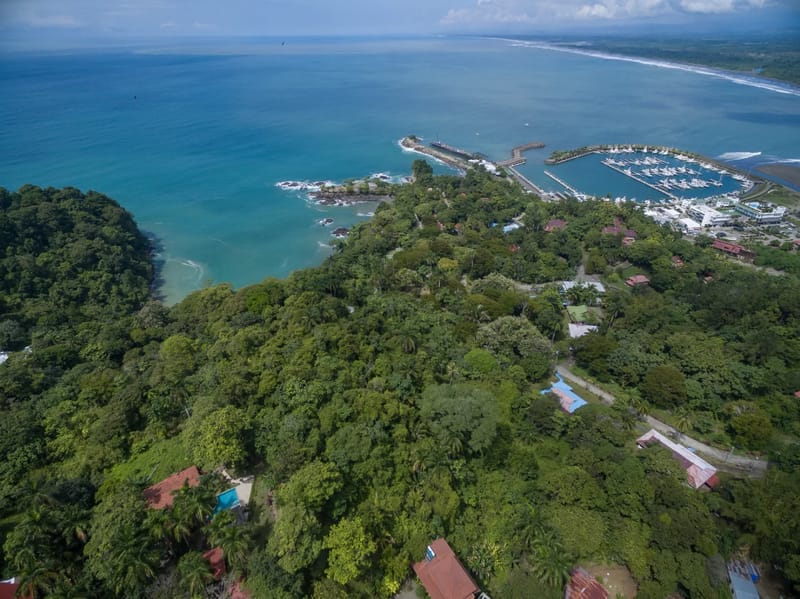 Casa Colibrí · 27. Una vista aérea muestra la amplia extensión del océano Pacífico de color turquesa, una exuberante selva tropical, una concurrida marina y villas dispersas entre el paisaje verde.