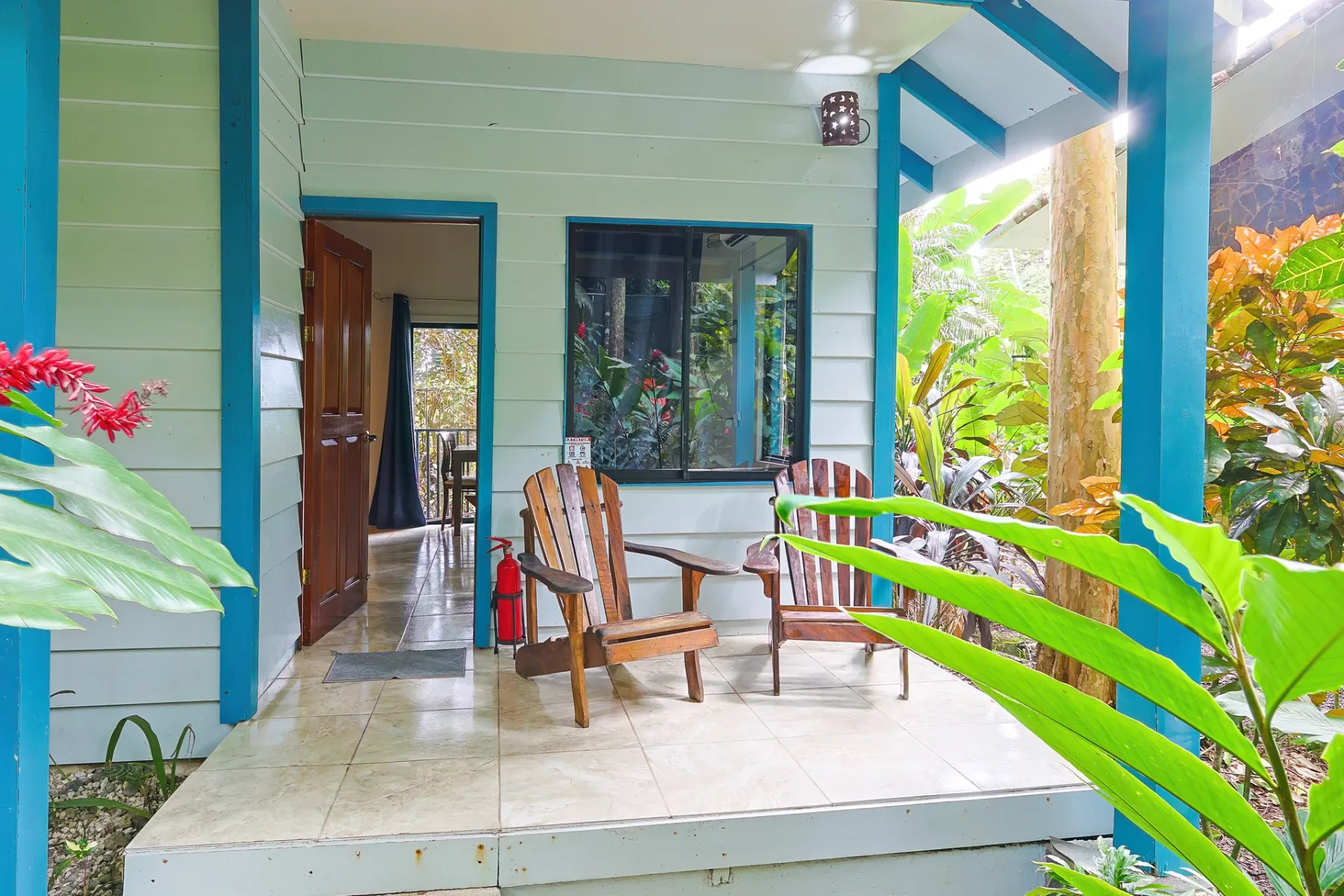 Un patio cubierto con asientos de madera se abre a una frondosa vegetación tropical.