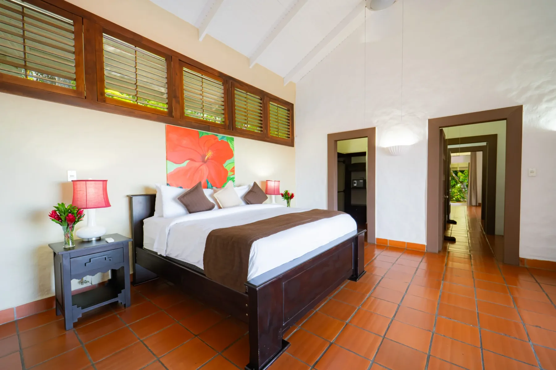 Dormitorio con una cama, mesitas de noche y ventanas altas.