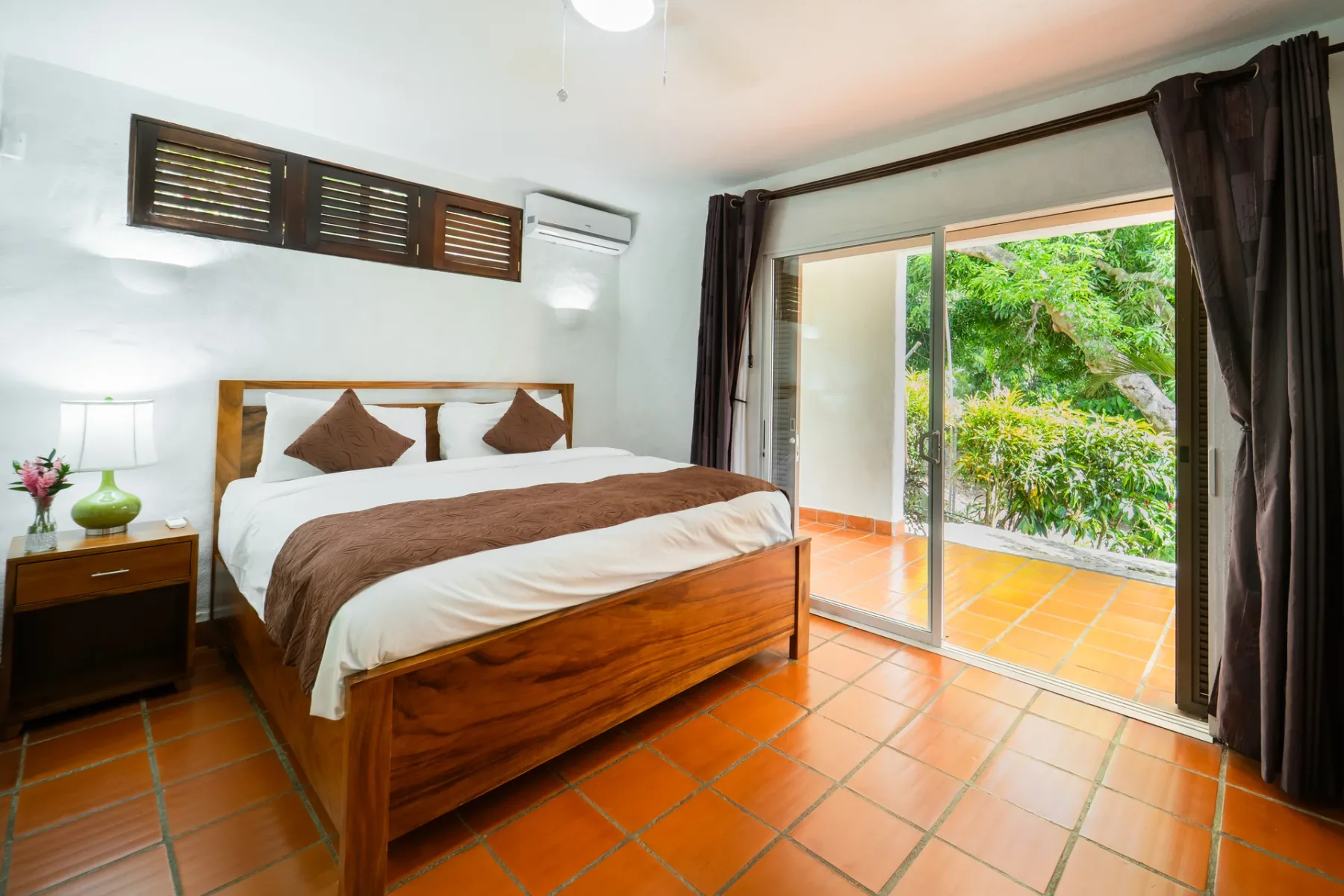 Un dormitorio con una cama de madera junto a puertas corredizas abiertas hacia un patio frondoso.