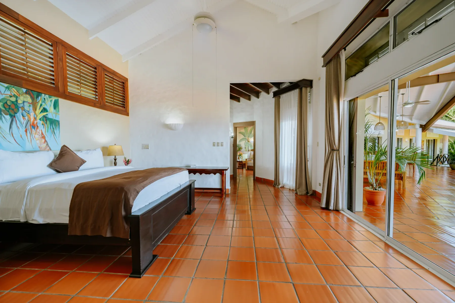 Un dormitorio con una cama junto a amplias puertas de vidrio que dan a un patio embaldosado.