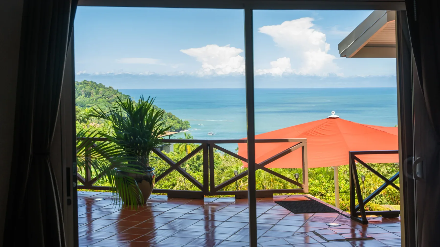 Una terraza de baldosas tiene vistas al mar azul y a un tejado rojo.