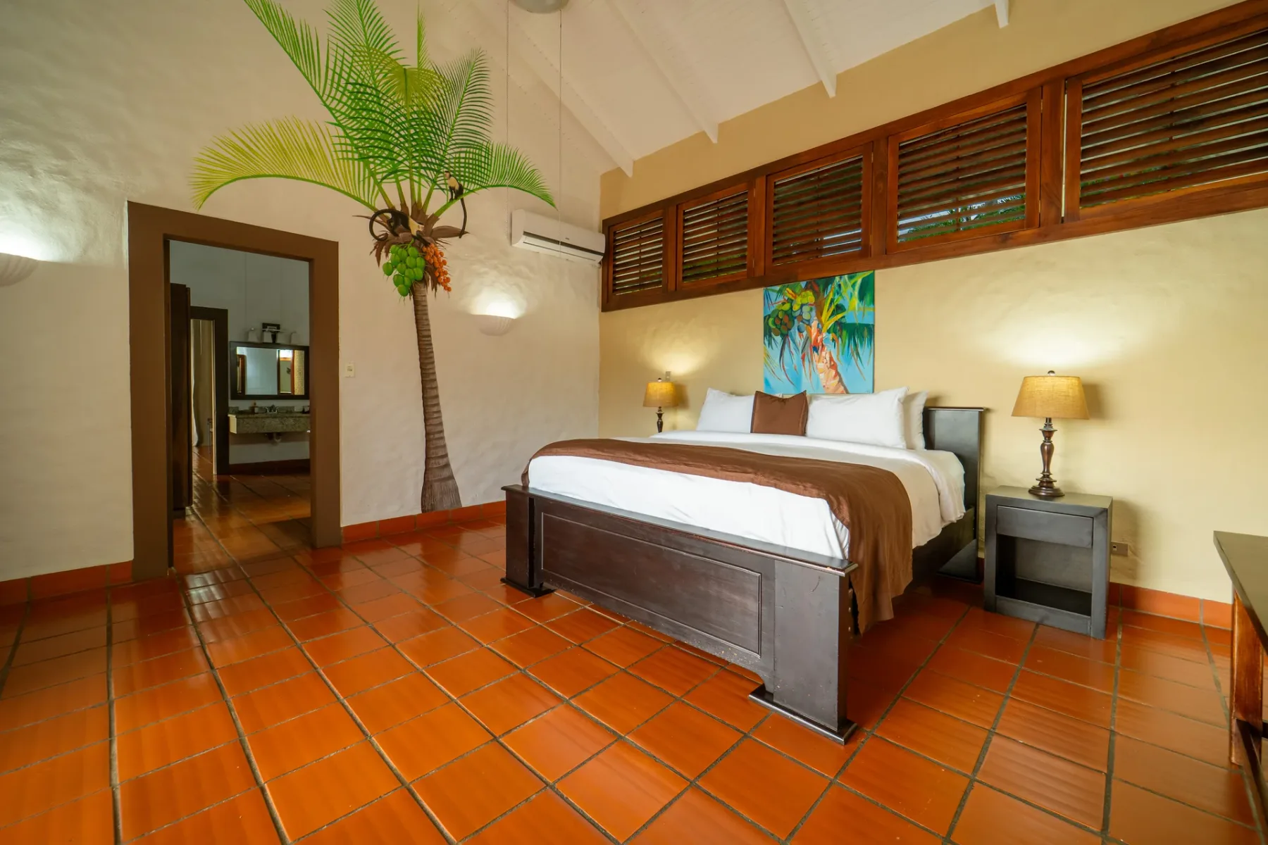 Un dormitorio con una cama, mesitas de noche y una palmera alta.
