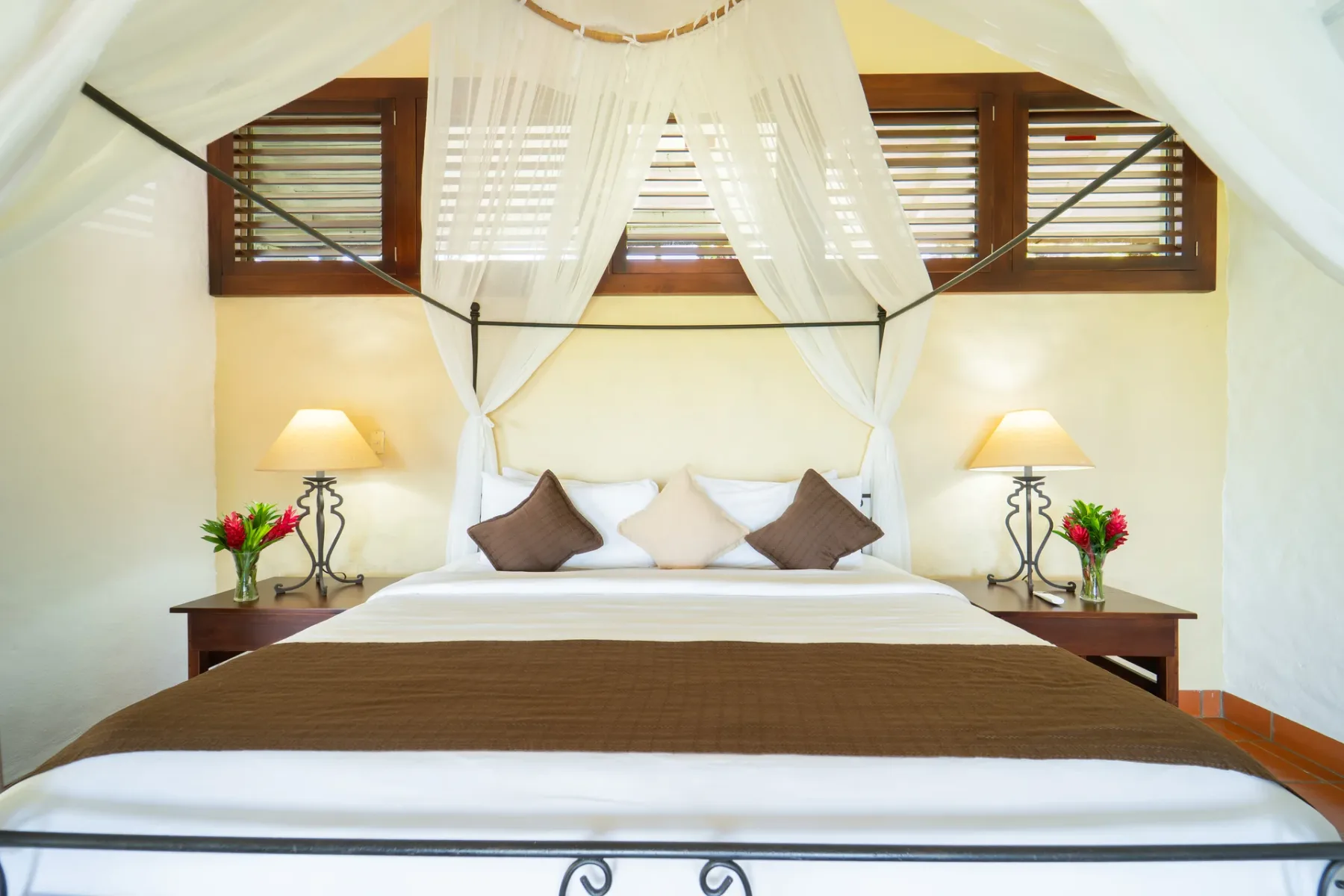 Un dormitorio con una cama con dosel, cojines decorativos y lámparas de noche.