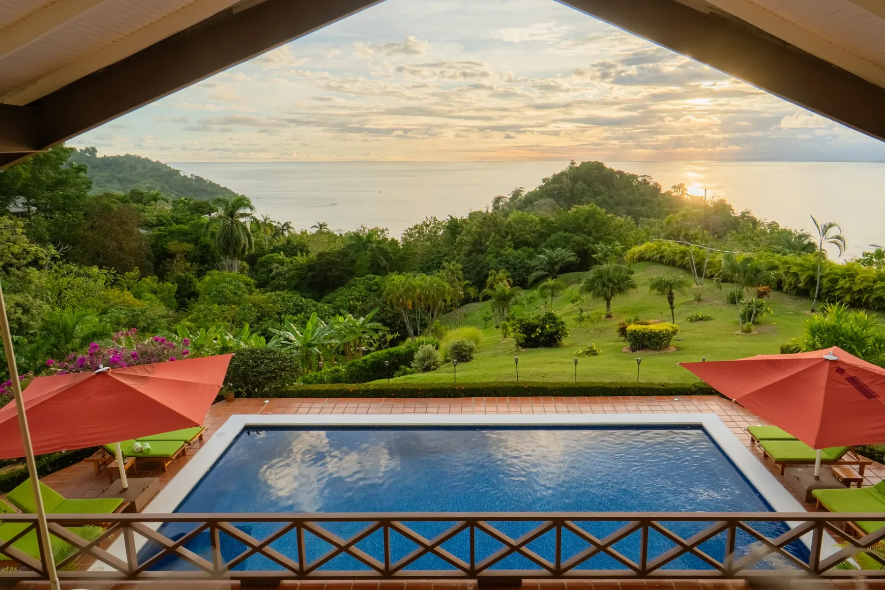 Una piscina da a jardines frondosos y al océano al atardecer.