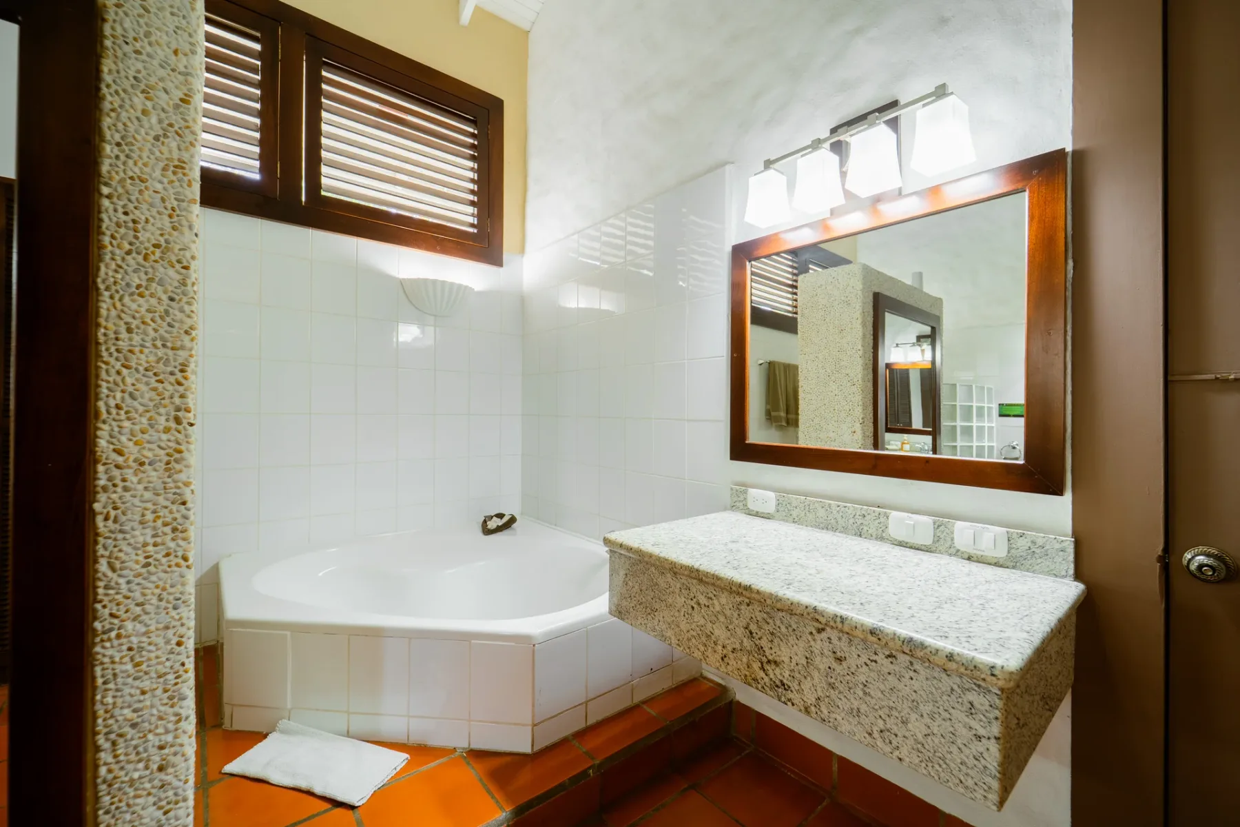Un baño con bañera esquinera, paredes alicatadas y un espejo grande.
