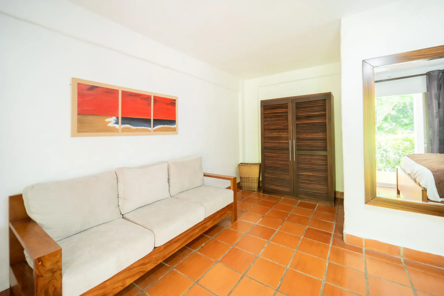 Una luminosa sala de estar con sofá acolchado, piso de baldosas y puertas de lamas de madera.
