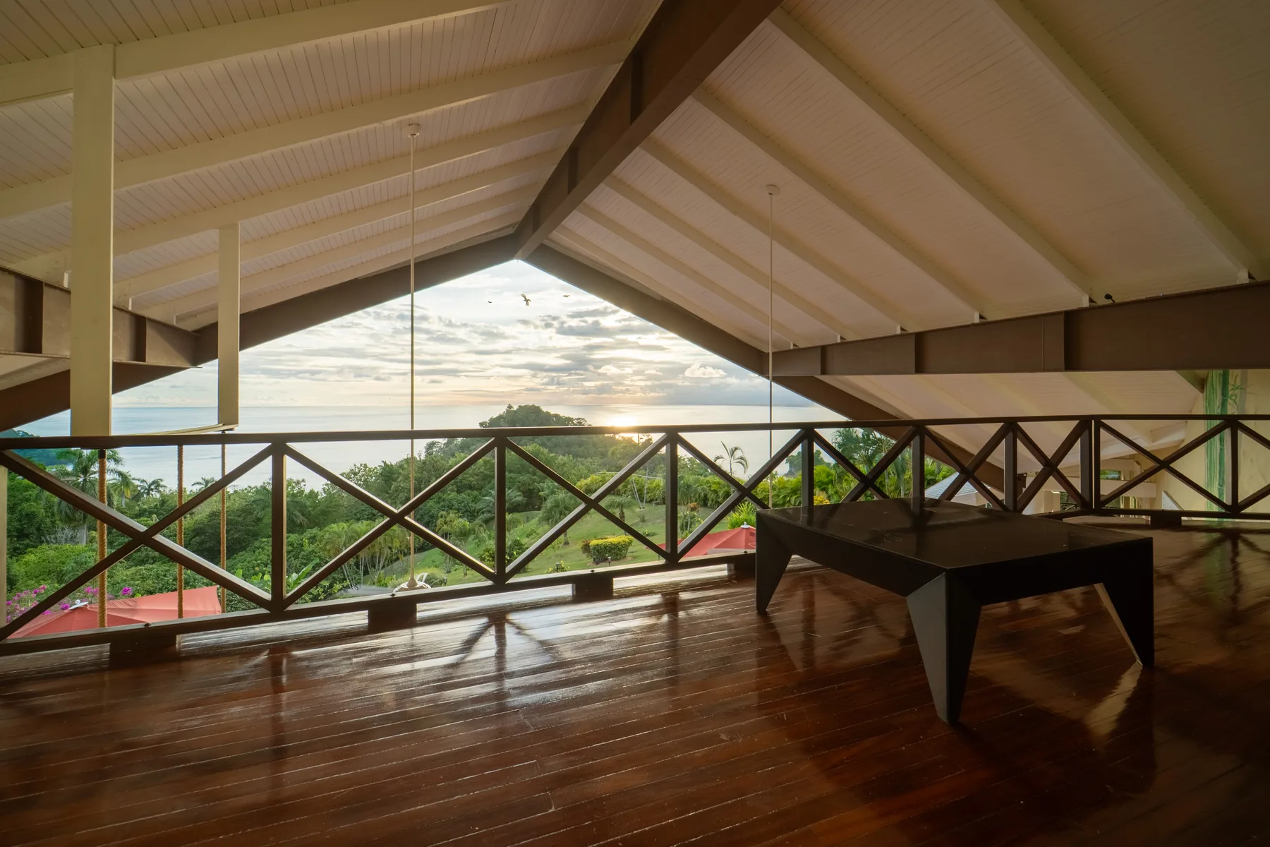 Una terraza cubierta de madera tiene vistas a árboles verdes y un paisaje soleado.