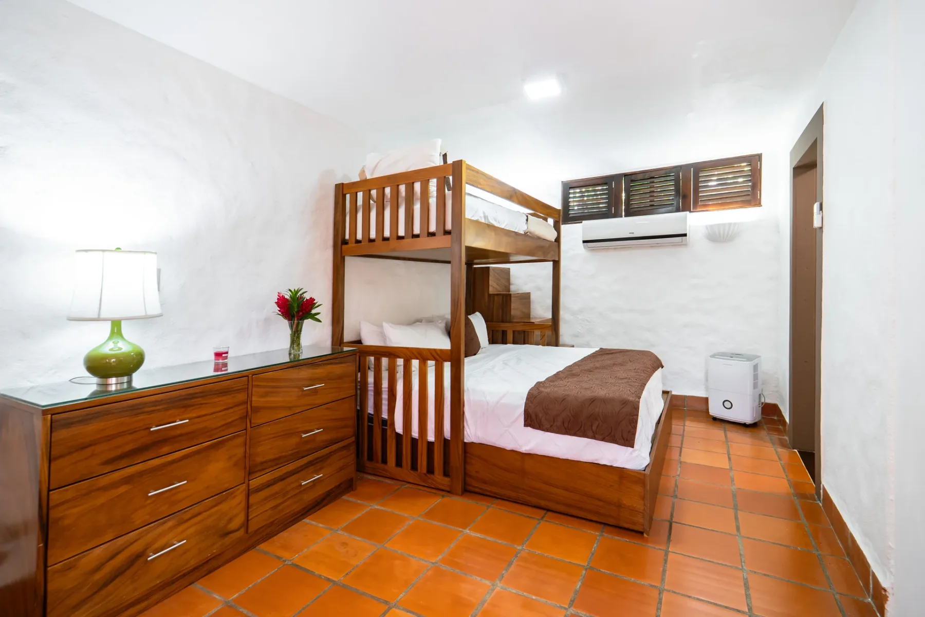 Un dormitorio con una litera de madera, una cómoda y suelo de baldosas.