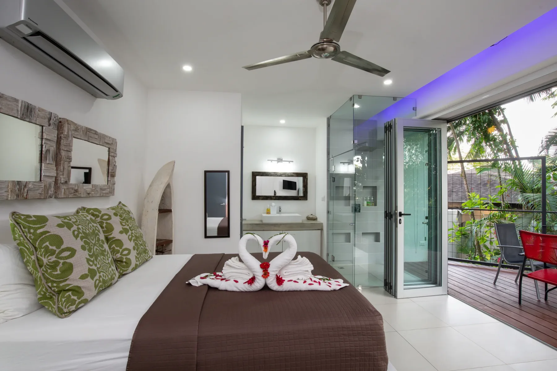 Un dormitorio con cama, cojines decorativos y una ducha de vidrio junto a un patio exterior.