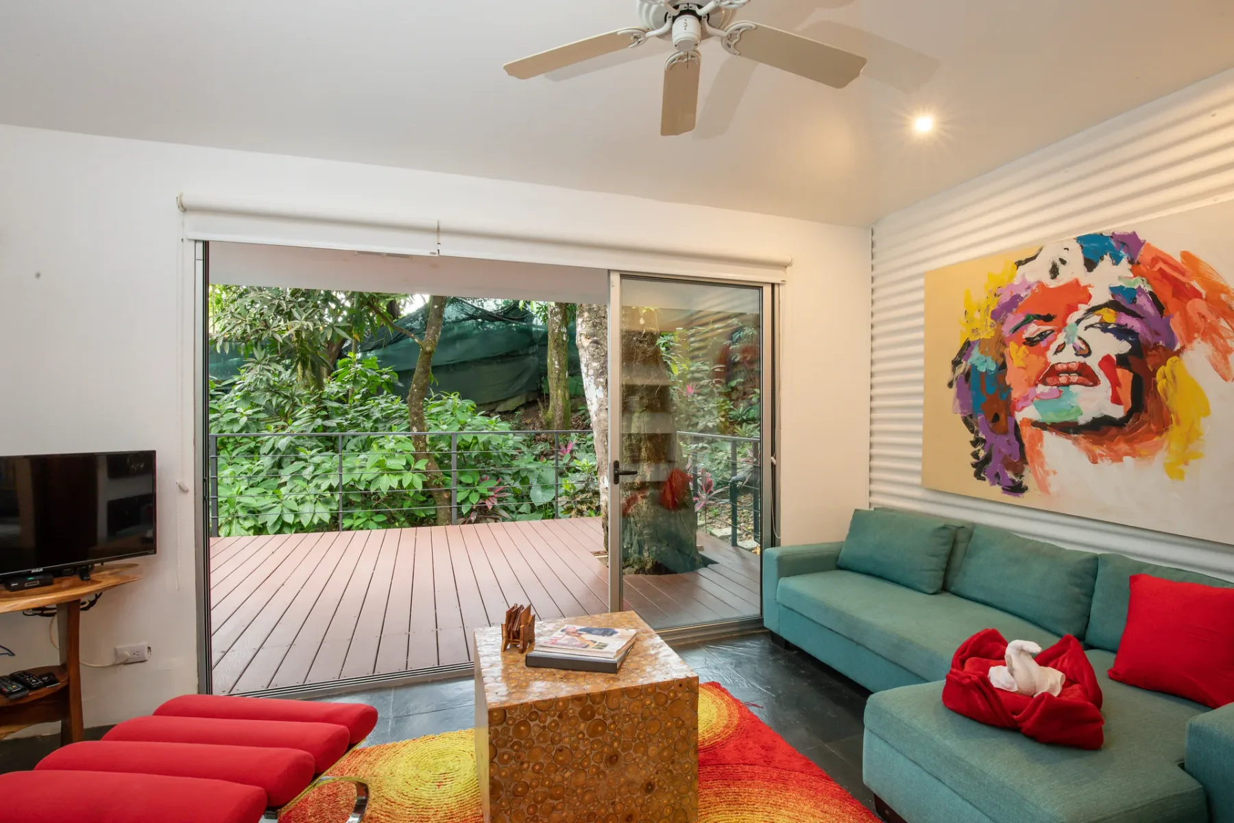 Una sala de estar con asientos color turquesa, arte colorido y puertas corredizas de vidrio hacia una terraza.