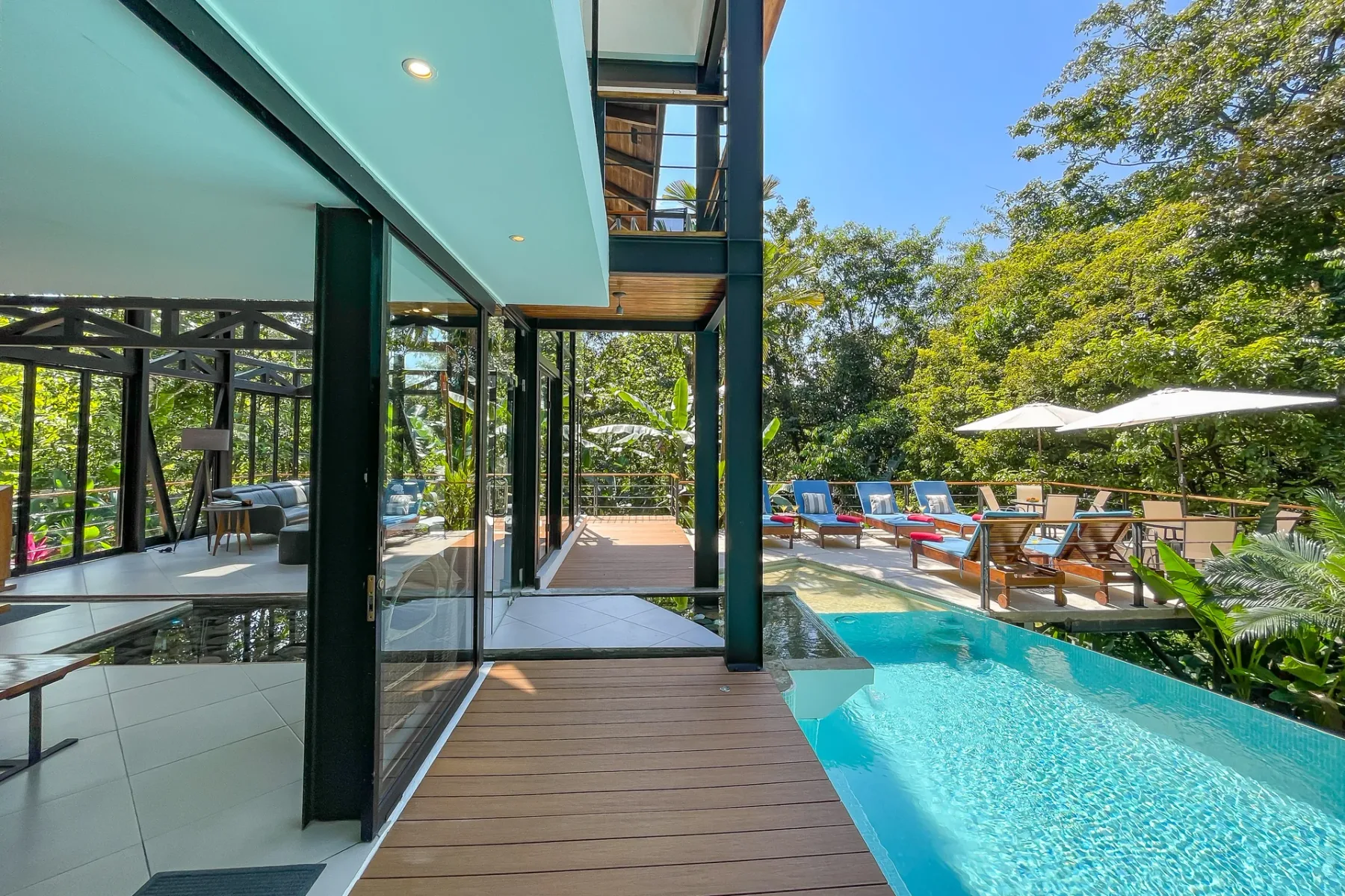 Una villa moderna con paredes de vidrio da a una terraza junto a la piscina con asientos al aire libre.