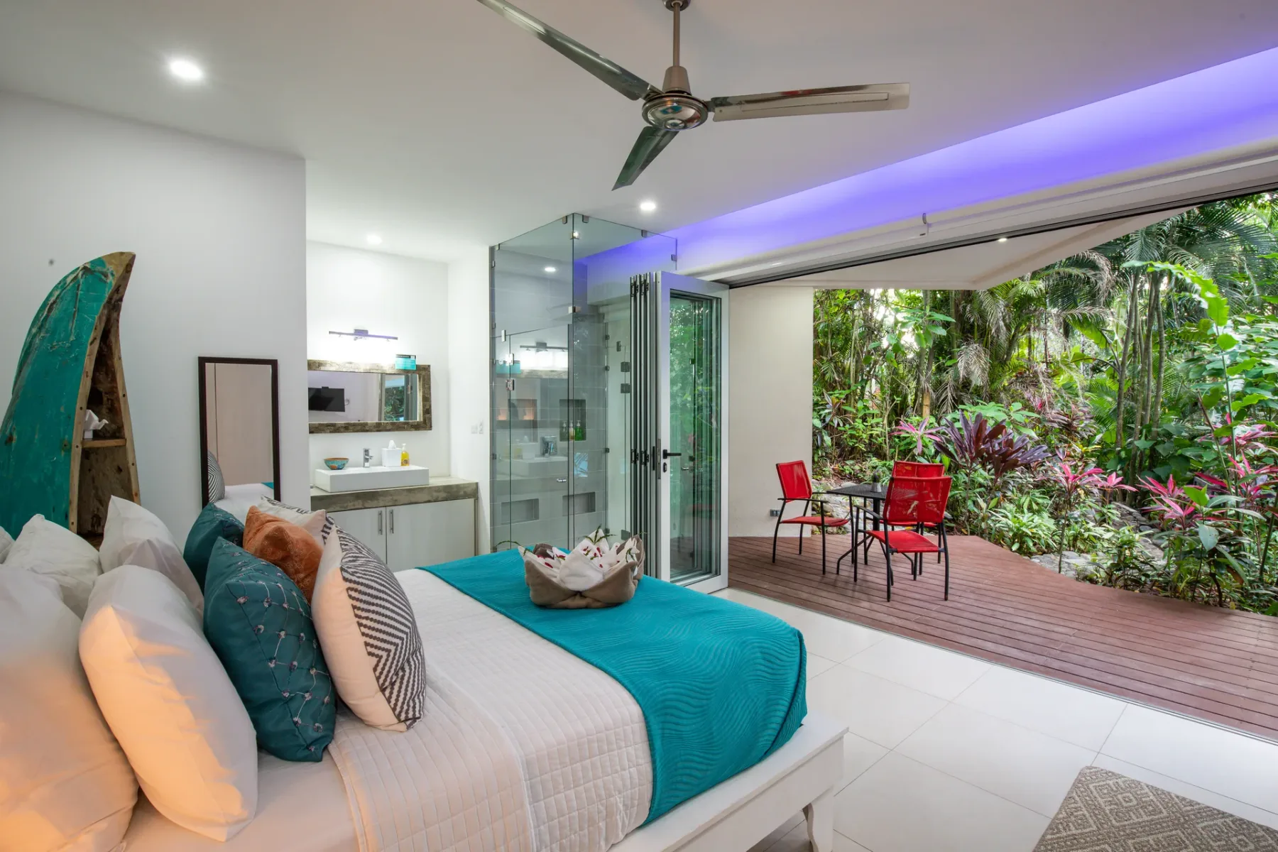 Un dormitorio se abre a un patio con asientos rojos y vegetación tropical.