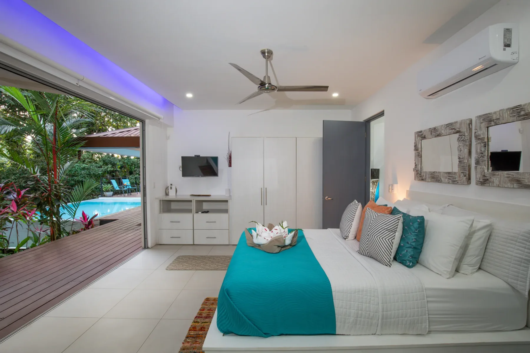 Un dormitorio luminoso se abre a una terraza de madera y un jardín con piscina.