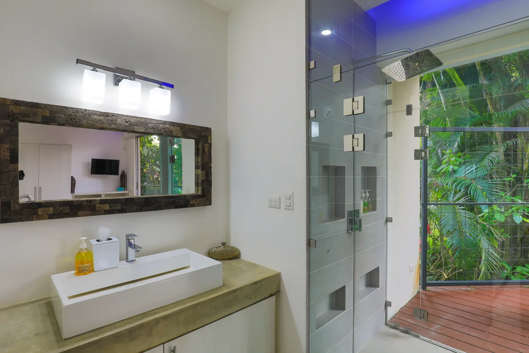 Un baño con lavabo sobre encimera y ducha de vidrio junto a una ventana con vista a la vegetación.
