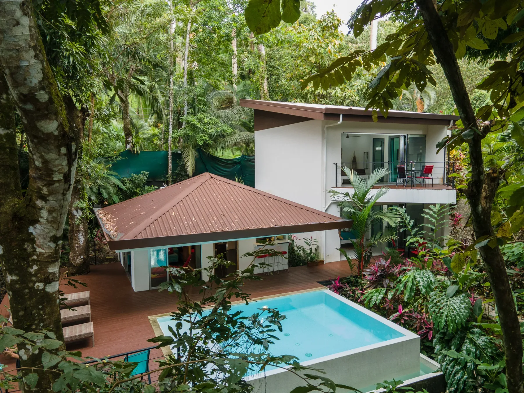 Una villa moderna rodeada de vegetación tropical, con una piscina en primer plano.