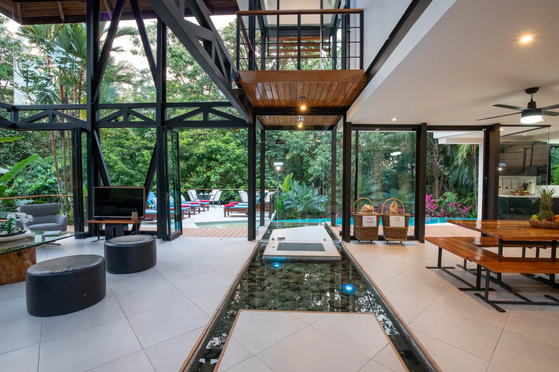 Una sala de estar y comedor de planta abierta da a un jardín frondoso a través de paredes de vidrio.