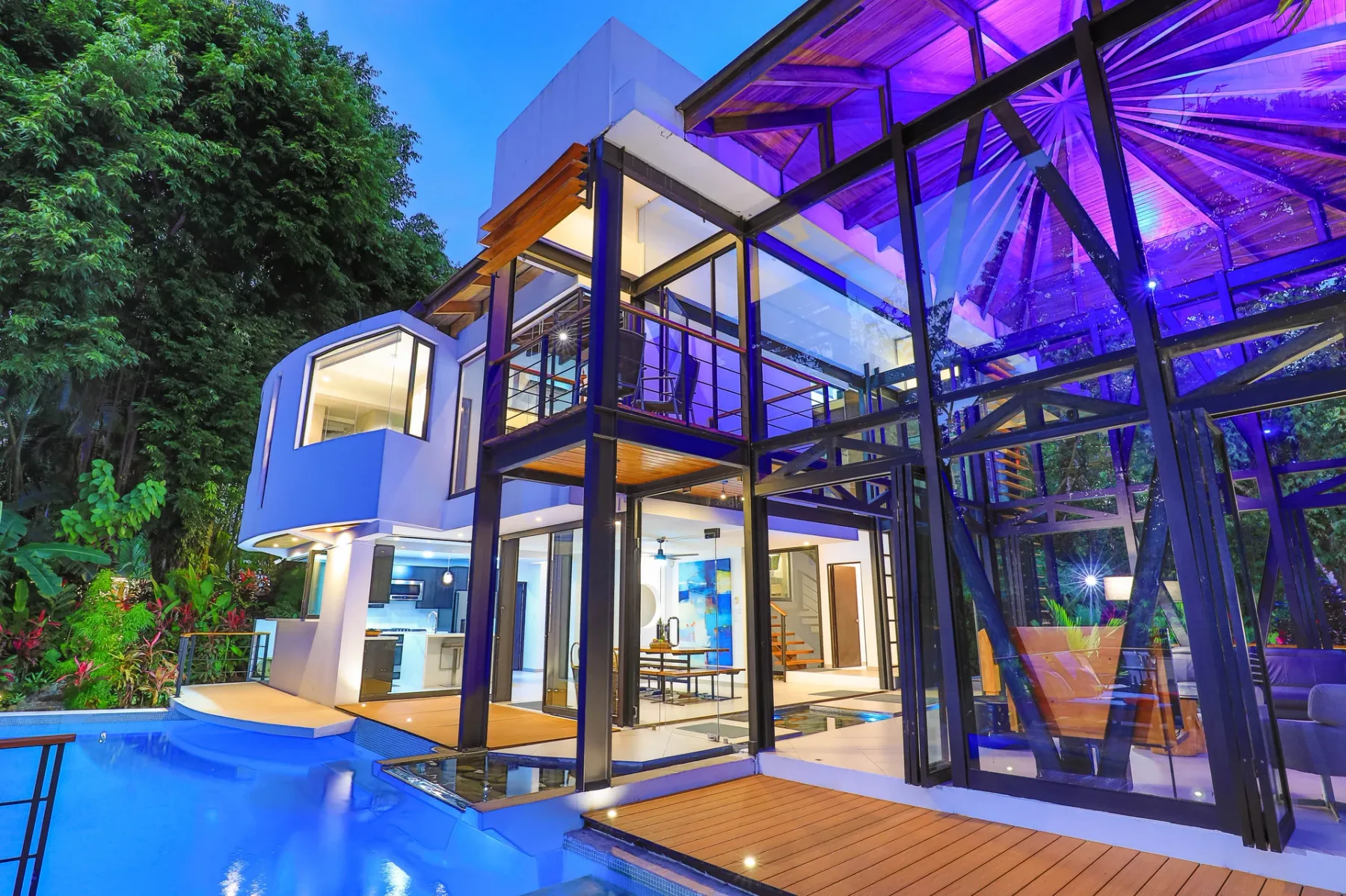 Una casa moderna con paredes de vidrio da a una piscina y una terraza de madera.
