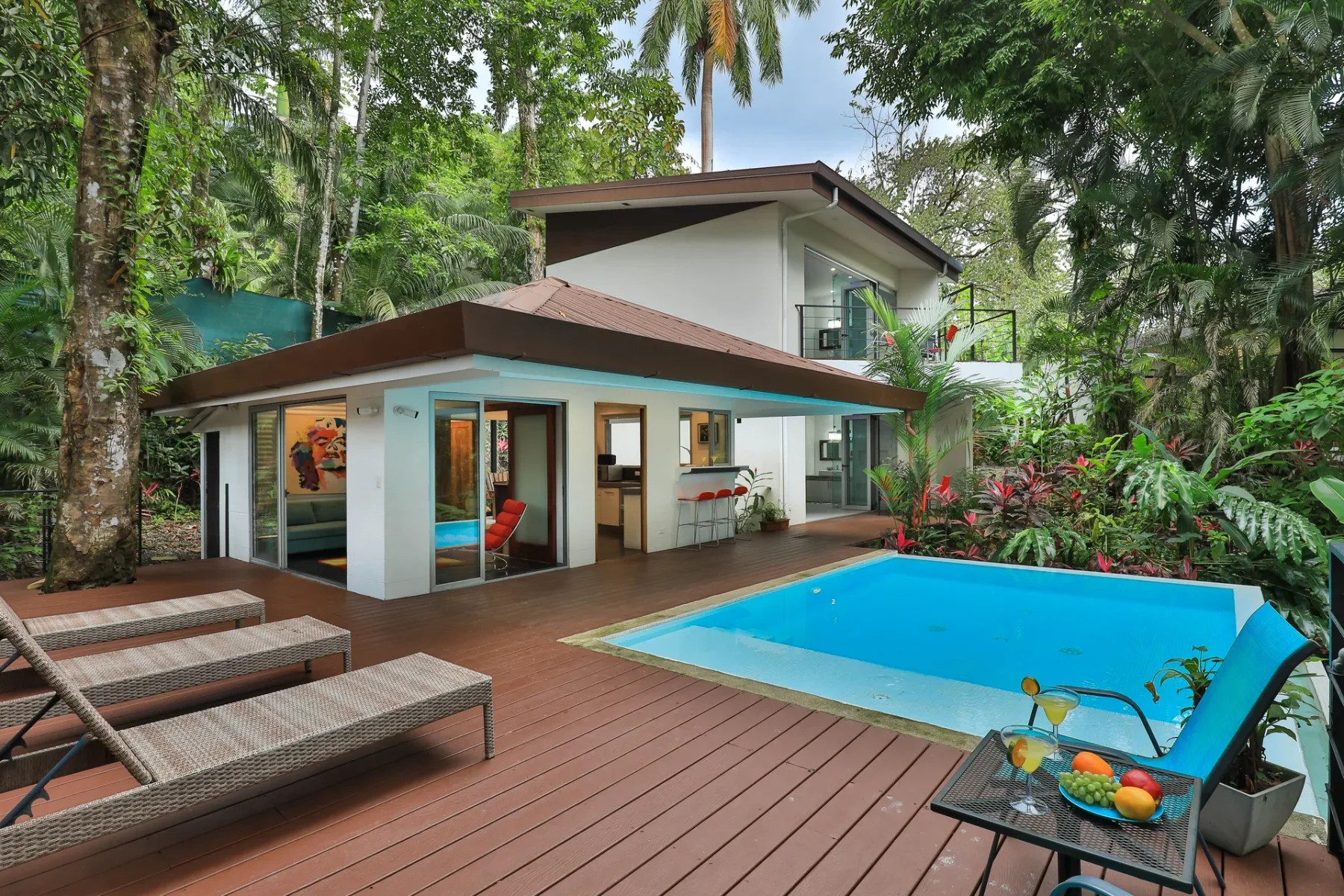 Una villa moderna se abre a una terraza de madera y una piscina azul.