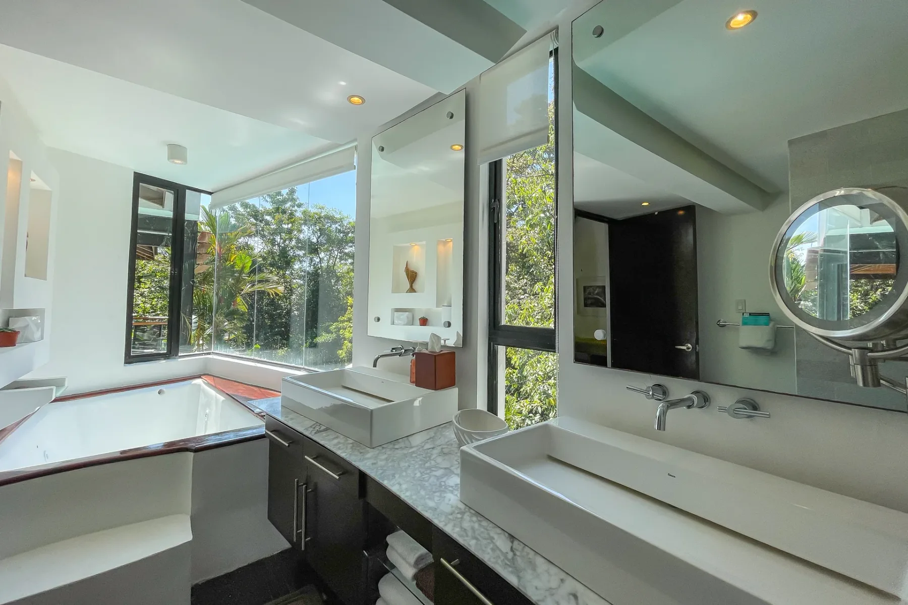 Un baño luminoso con una encimera larga y grandes ventanas con vistas a la vegetación.