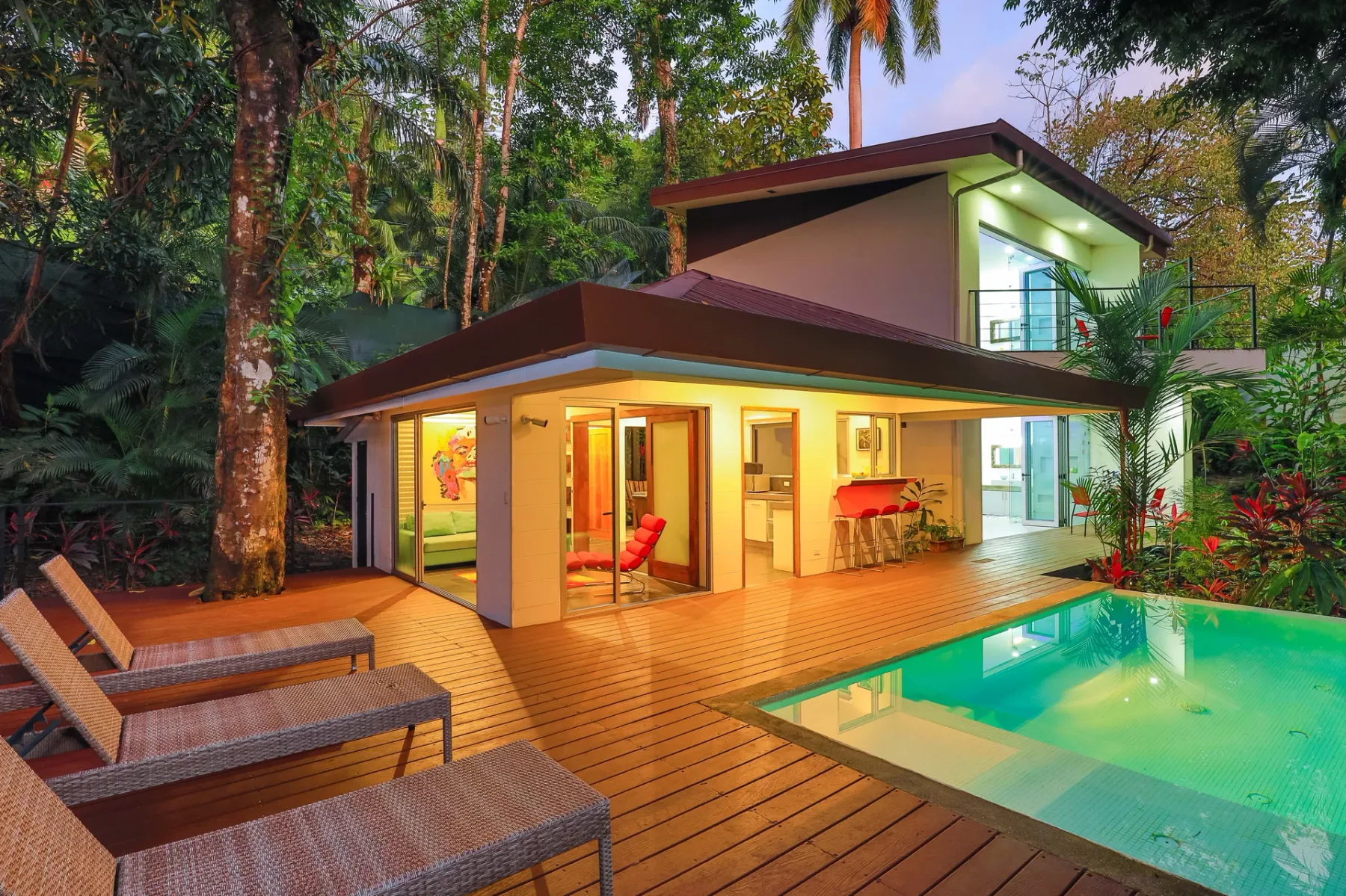 Una casa moderna se abre a una terraza de madera junto a una piscina.