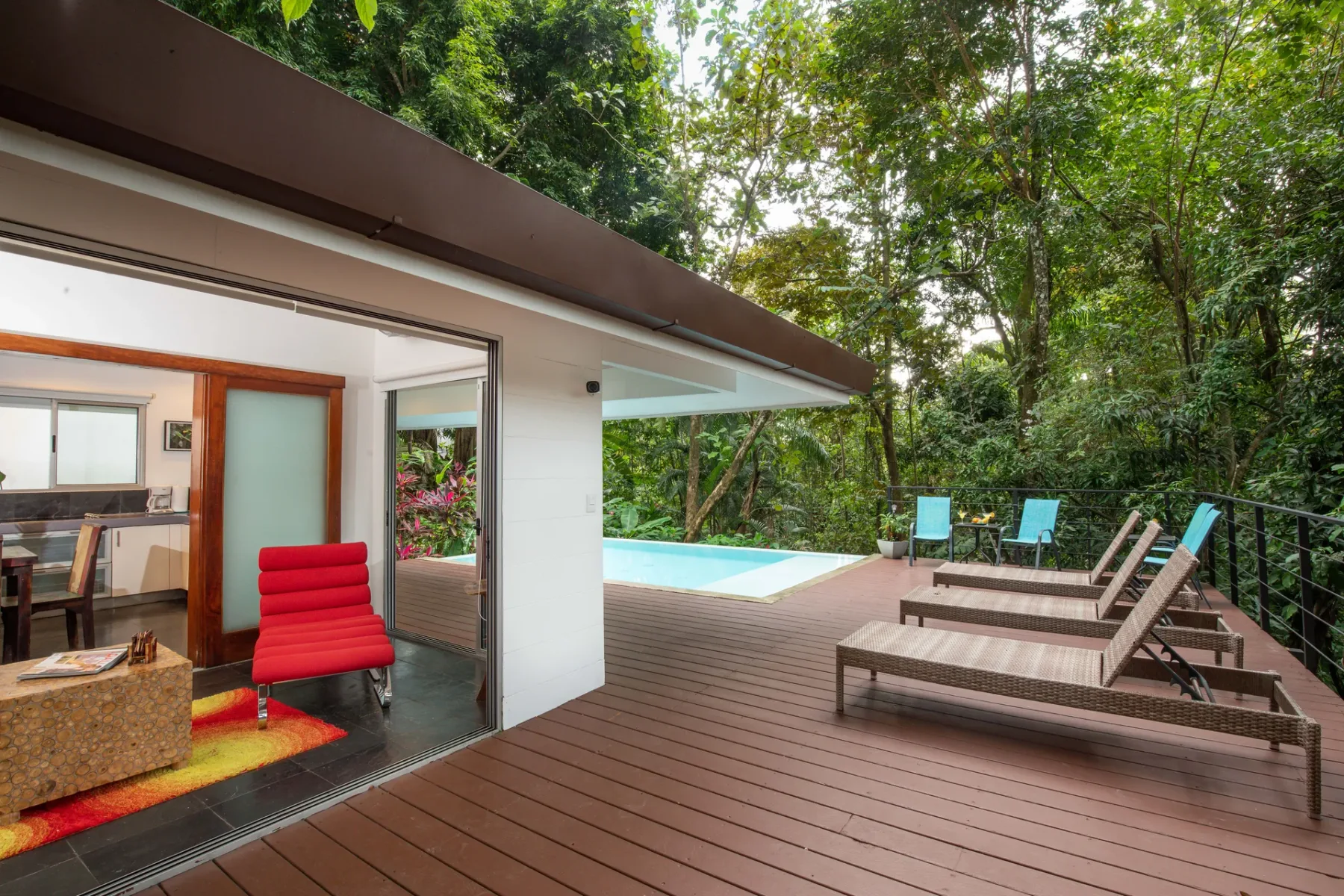 Una terraza junto a una villa moderna tiene asientos junto a la piscina y árboles alrededor.
