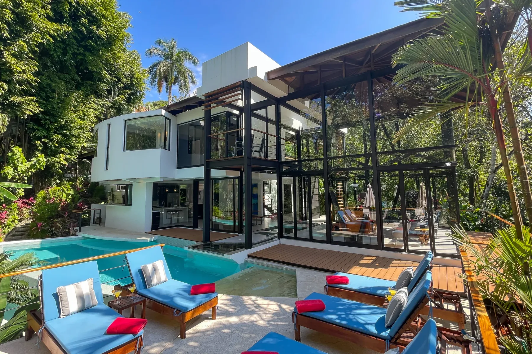 Una villa moderna con fachada de vidrio da a una piscina con asientos azules.