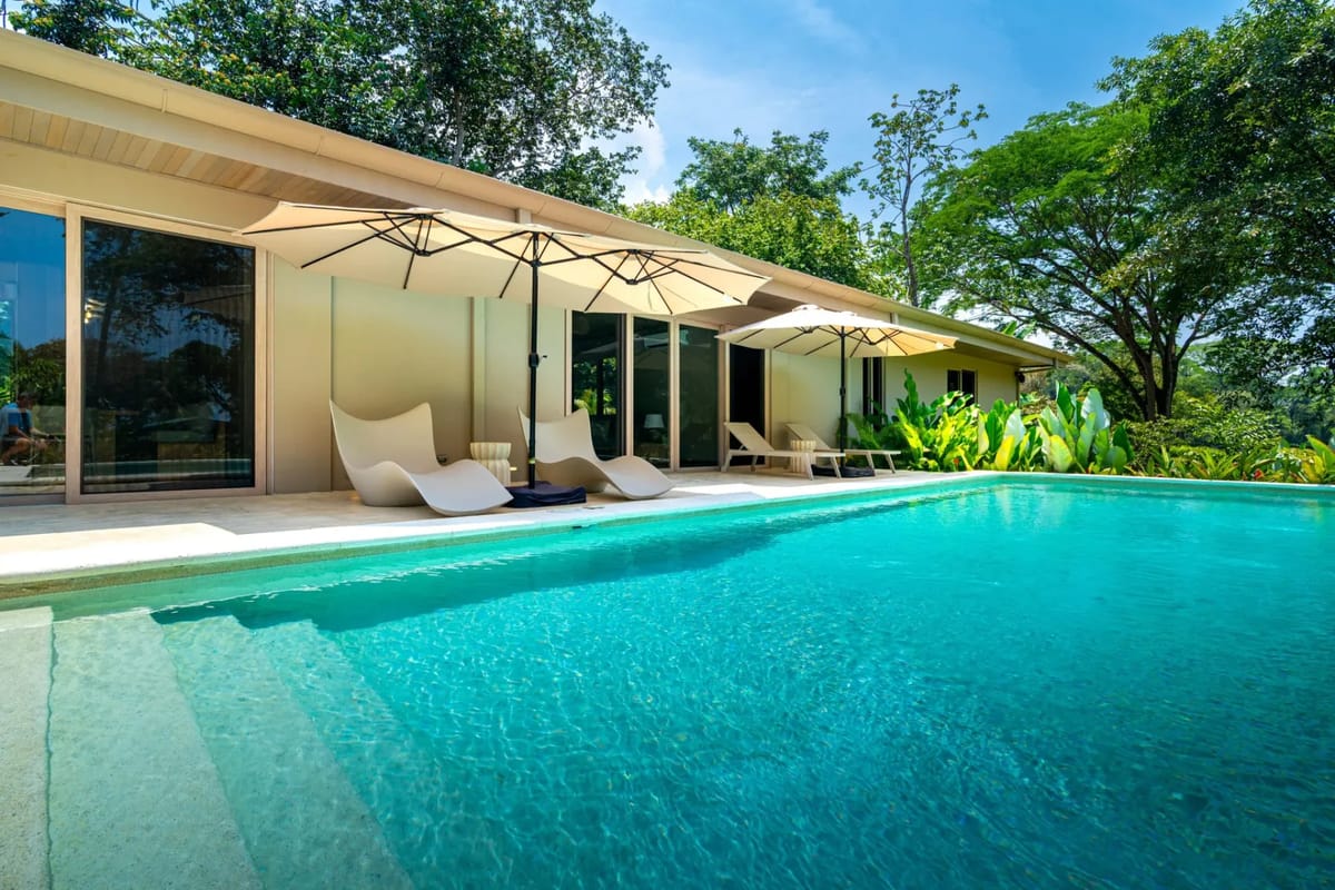 Chalet Tropical · 14. A private outdoor pool is adjoined by a patio with sun loungers and umbrellas, situated next to the villa's large glass doors and surrounded by abundant tropical trees.
