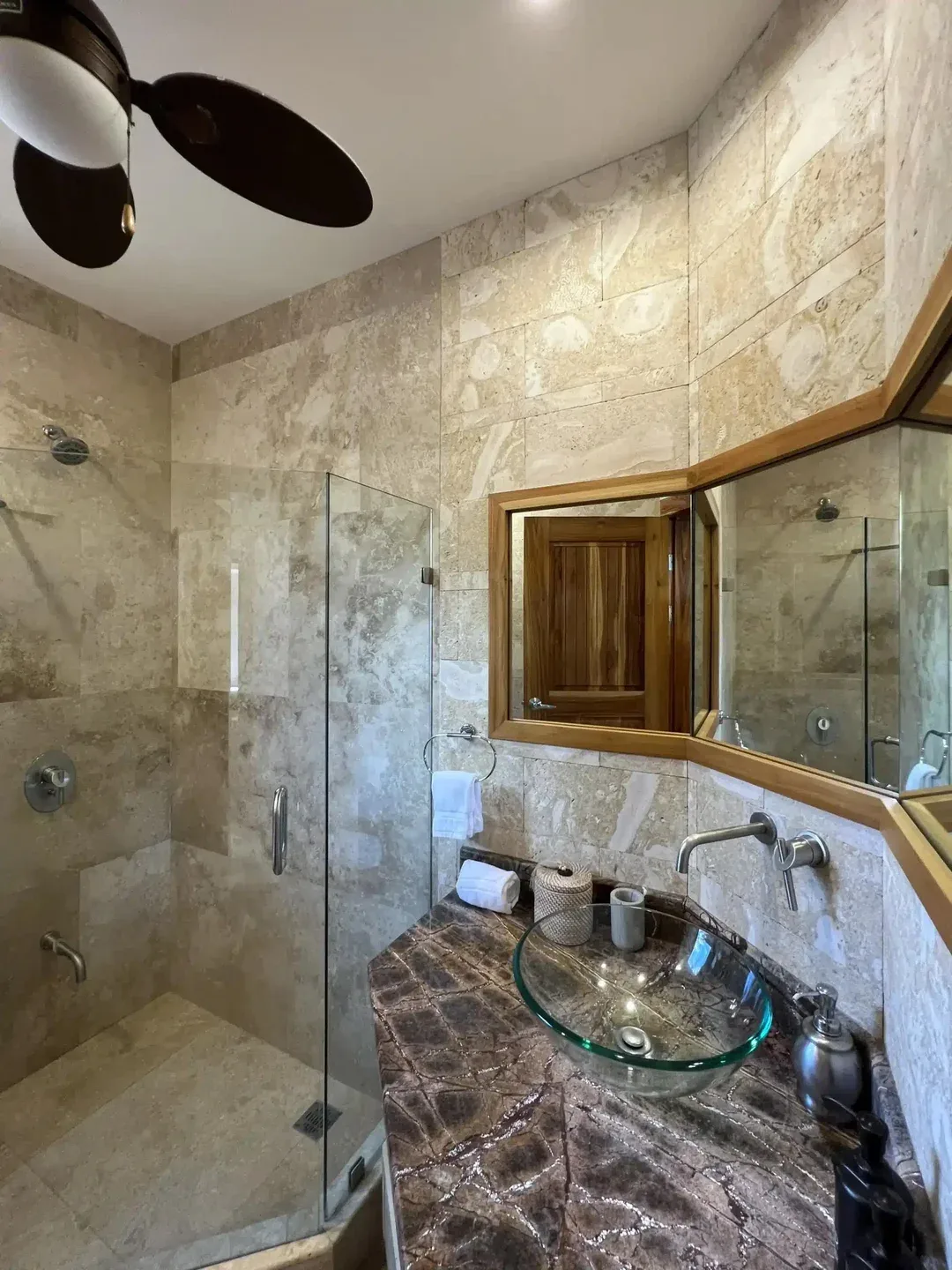 A tiled bathroom has a glass shower and a vessel sink on a dark countertop.
