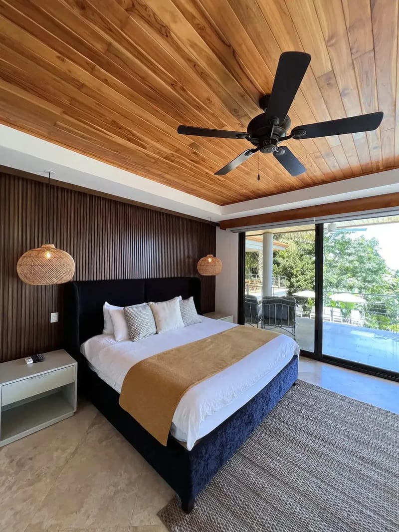 Casa Anjali Luxury Villa · 45. A bedroom with a king bed, a vaulted teak ceiling with a fan, and floor-to-ceiling glass doors that open to a private terrace overlooking the tropical rainforest.