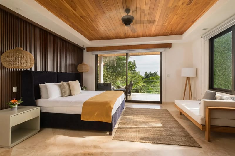 Casa Anjali Luxury Villa · 52. A king bedroom features a teak paneled ceiling and a wood-slatted accent wall, with floor-to-ceiling glass doors providing natural light and rainforest views from the private terrace.
