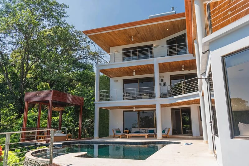Casa Anjali Luxury Villa · 10. The multi-level villa includes an infinity pool and sun deck, set against a backdrop of tropical rainforest, with open-air terraces and glass doors connecting to spacious interiors.