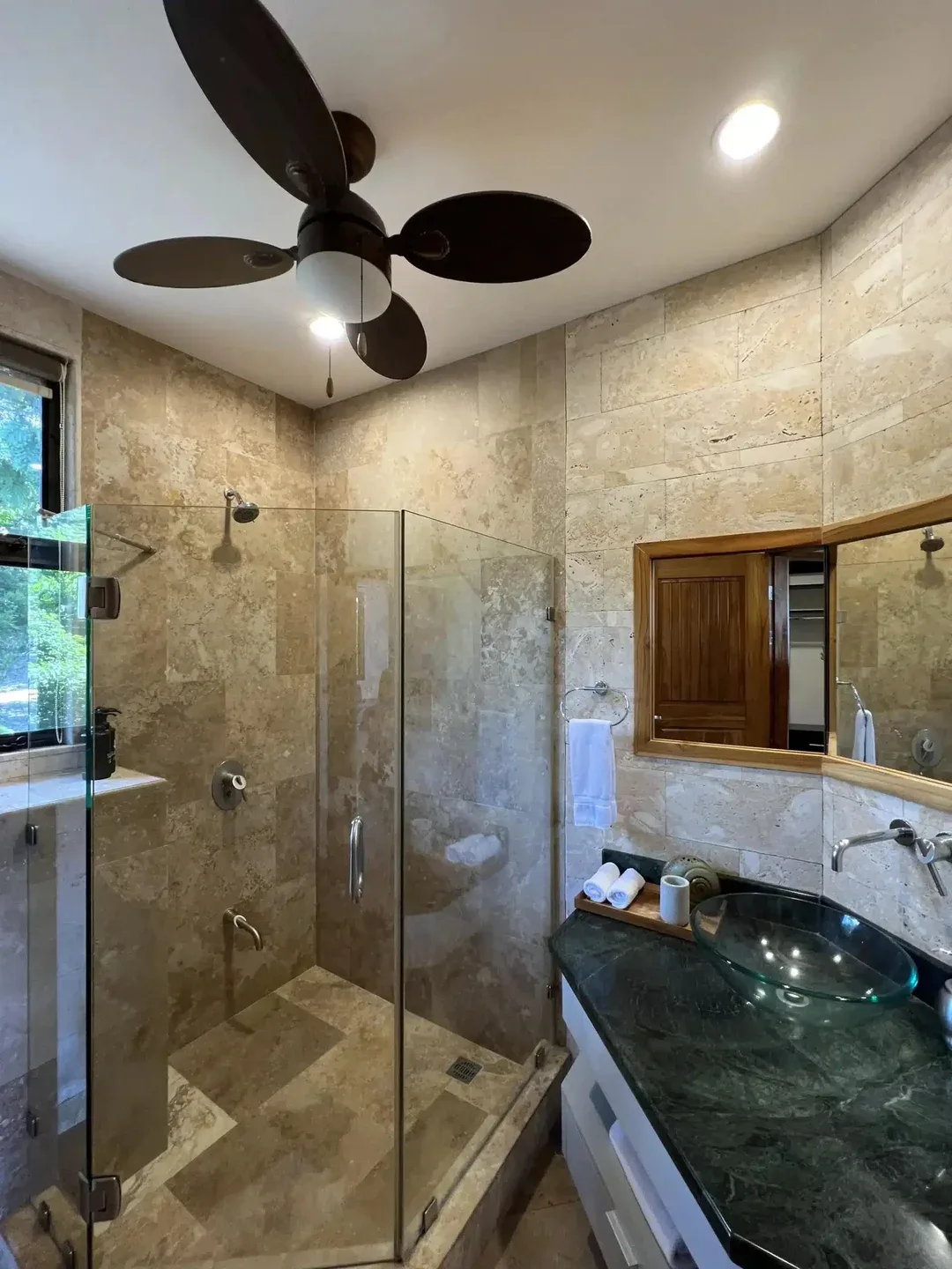 A bathroom with stone walls, a glass shower, and a dark vanity.