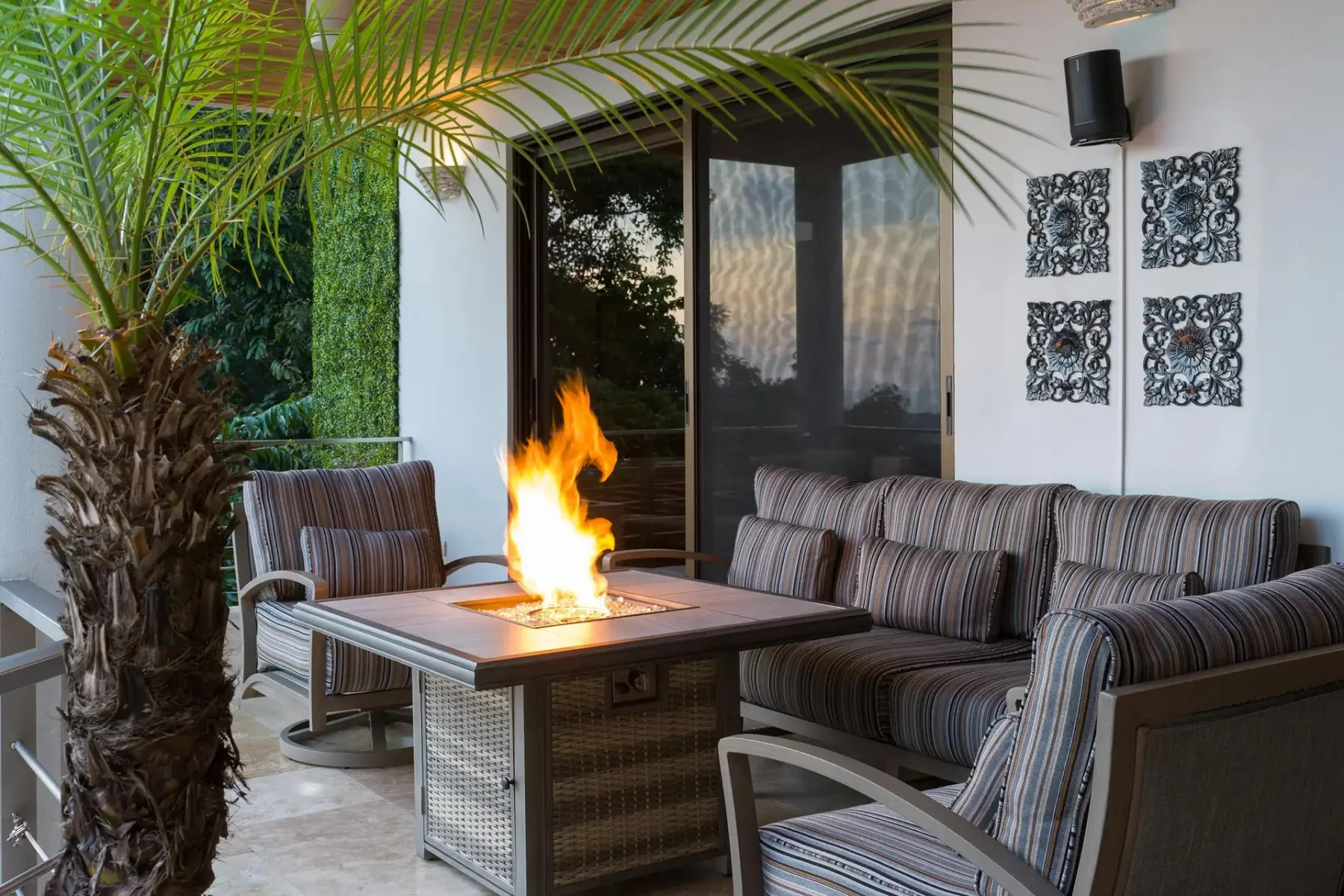 A covered terrace has striped seating arranged around a lit fire pit.