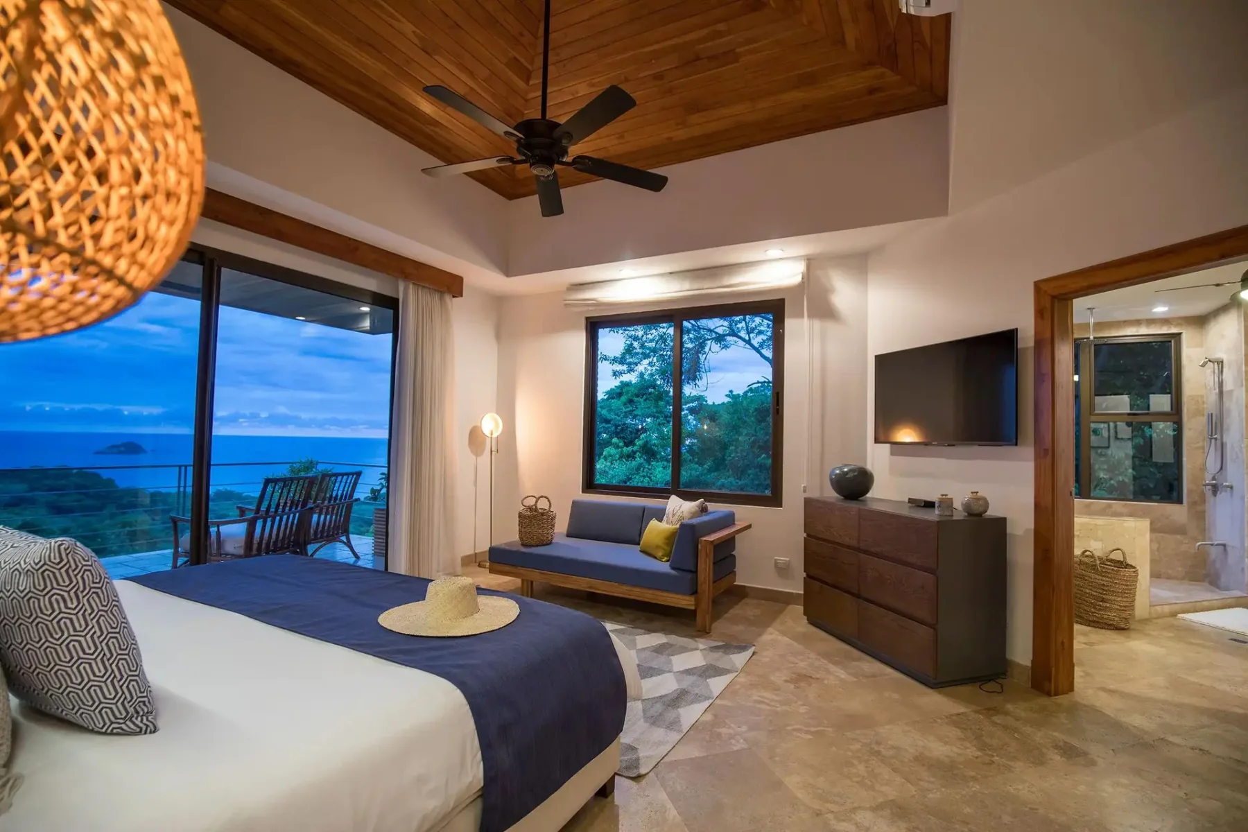 A bedroom with a bed, seating, and glass doors overlooking the ocean.