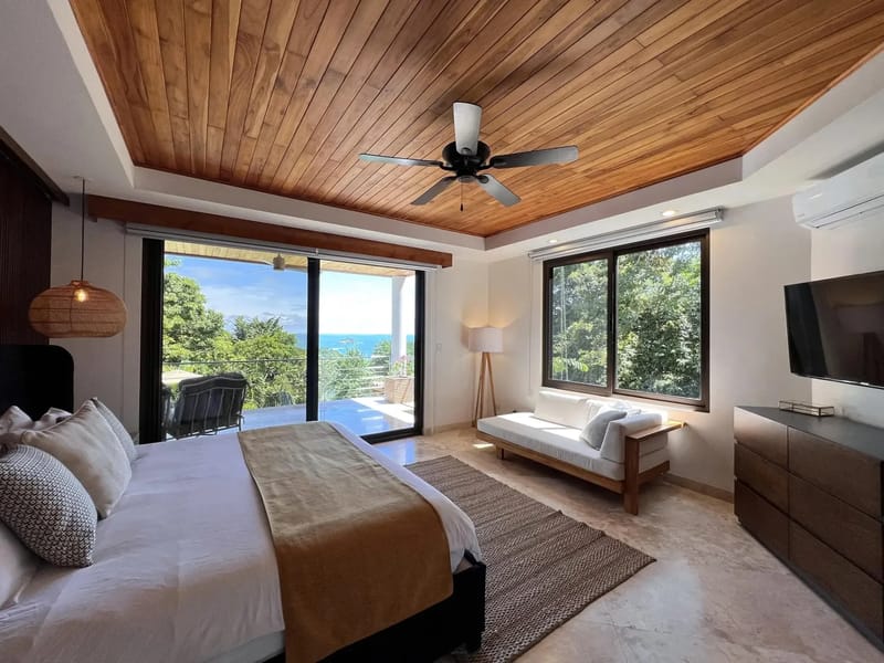 Casa Anjali Luxury Villa · 44. This bedroom features a vaulted teak ceiling, natural light, and floor-to-ceiling glass doors that open to a private terrace with ocean and rainforest views.