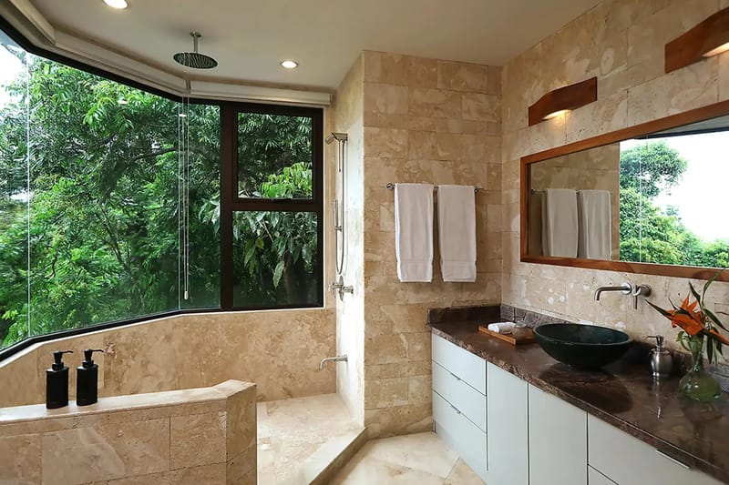 Casa Anjali Luxury Villa · 35. The natural stone bathroom features a walk-in shower and dual vanity, with expansive windows opening directly to rainforest views.